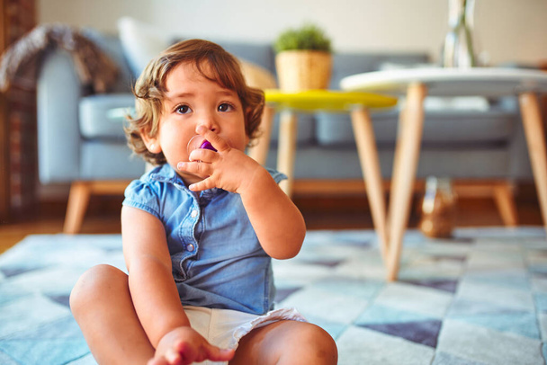 Kaunis lapsi lapsi tyttö yllään denim paita istuu matolla käyttäen tutti
 - Valokuva, kuva