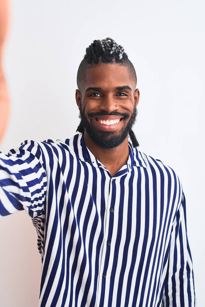 Afrykański Amerykanin z warkoczami zrobić selfie przez kamerę na odizolowanym białym tle ze szczęśliwą twarzą stoi i uśmiecha się z pewnym uśmiechem pokazując zęby - Zdjęcie, obraz