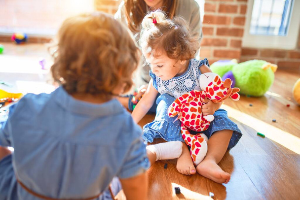 Kaunis opettaja ja ryhmä pikkulapsia leikkimässä paljon leluja päiväkodissa
 - Valokuva, kuva