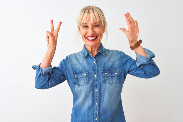 Žena středního věku na sobě ležérní džínové košile stojící nad izolovaným bílým pozadím ukazující a ukazující prsty číslo sedm a usmívající se sebevědomě a šťastně. - Fotografie, Obrázek
