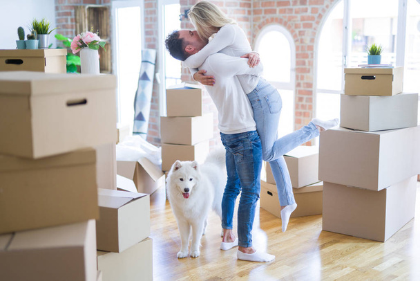 Jong mooi paar met hond knuffelen bij nieuw huis rond kartonnen dozen - Foto, afbeelding