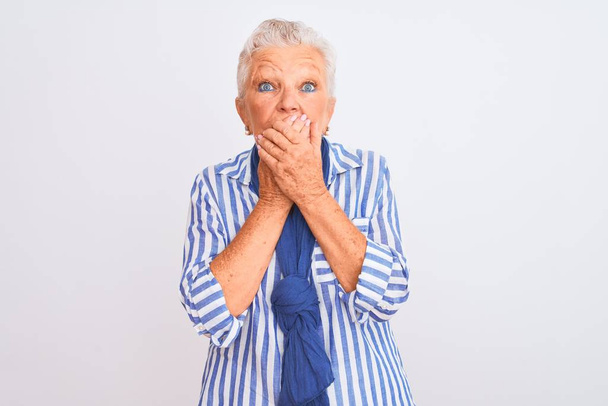 Femme âgée aux cheveux gris portant chemise à rayures bleues debout sur fond blanc isolé choqué couvrant la bouche avec les mains par erreur. Concept secret
. - Photo, image