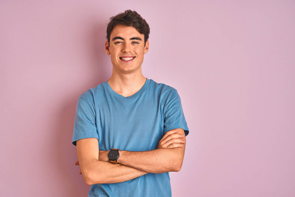 Menino adolescente vestindo camiseta casual em pé sobre fundo isolado azul rosto feliz sorrindo com os braços cruzados olhando para a câmera. Pessoa positiva
. - Foto, Imagem
