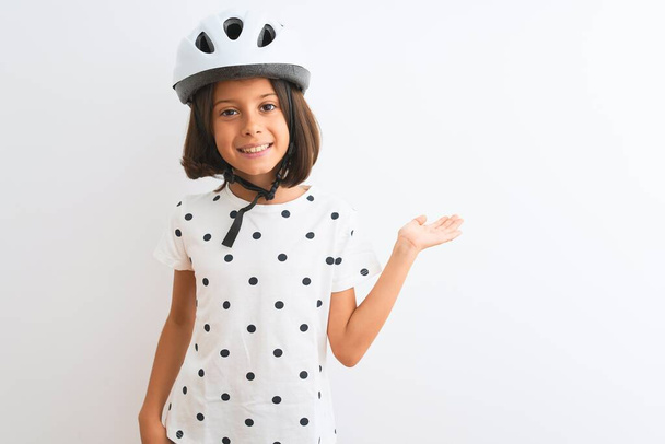 Красива дівчина в шоломі безпечного велосипеда, що стоїть над ізольованим білим тлом, усміхнений веселий подарунок і вказує долонею, дивлячись на камеру
. - Фото, зображення