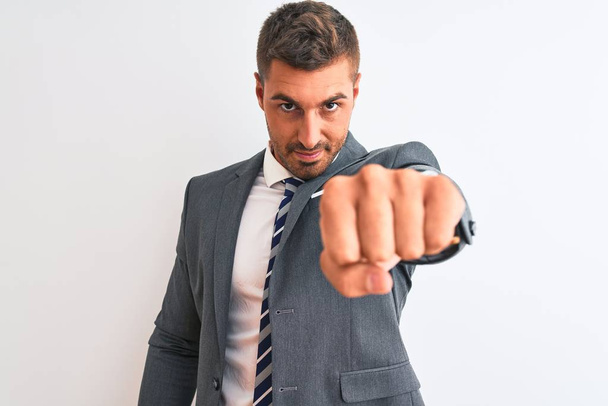 Young handsome business man wearing suit and tie over isolated background Punching fist to fight, aggressive and angry attack, threat and violence - Foto, Imagen