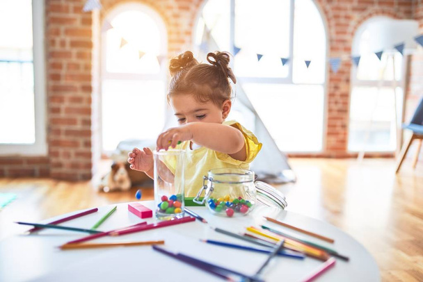 Bela criança de pé brincando com bolas coloridas de chocolate na mesa no jardim de infância
 - Foto, Imagem