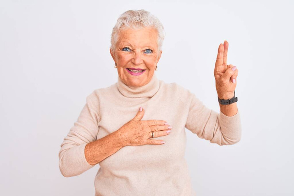 Donna anziana dai capelli grigi indossa maglione dolcevita in piedi sopra isolato sfondo bianco sorridente giurando con mano sul petto e le dita in su, facendo un giuramento di fedeltà
 - Foto, immagini