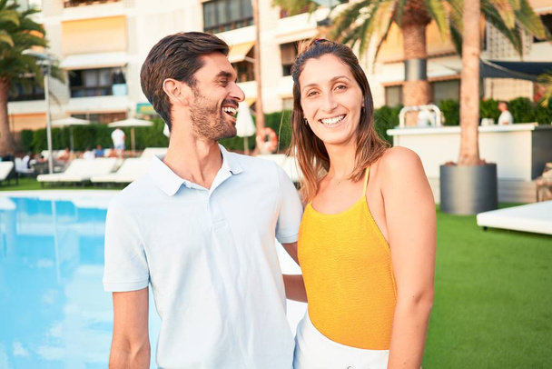Tatilde mutlu ve kendinden emin gülümseyen genç bir çift. Yüzünde tebessümle plaj kulübünde sarılırken - Fotoğraf, Görsel