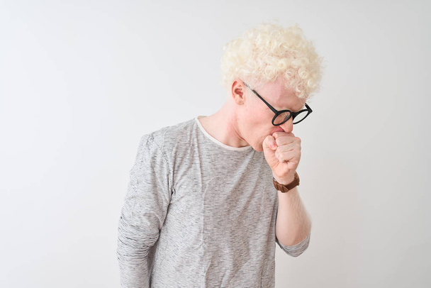 Mladý albín blond muž nosí pruhované tričko a brýle přes izolované bílé pozadí pocit nevolnosti a kašel jako symptom pro nachlazení nebo zánět průdušek. Koncept zdravotní péče. - Fotografie, Obrázek