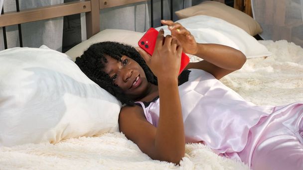 pretty young woman in pajamas lies in bed takes smartphone - Photo, Image