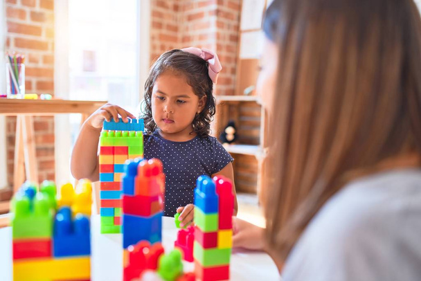 Красива вчителька і дівчинка-малюк грає з будівельними блоками, що забивають вежу в дитячому саду
 - Фото, зображення