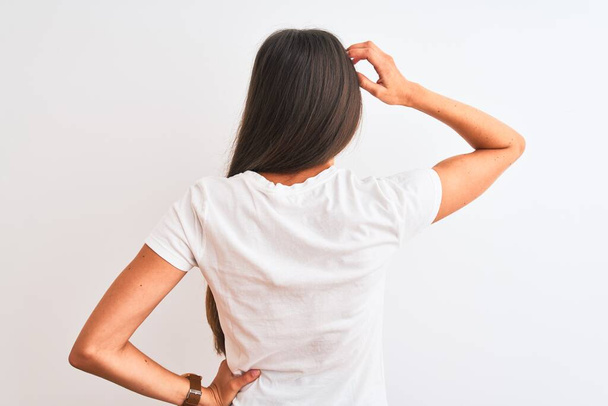 Young beautiful woman wearing casual t-shirt standing over isolated white background Backwards thinking about doubt with hand on head - Zdjęcie, obraz