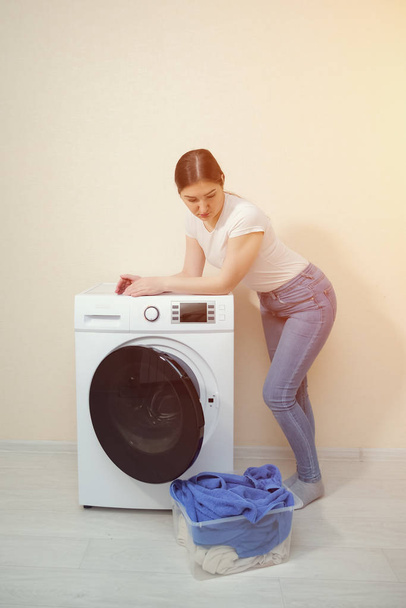 housewife leaning on washing machine looks at laundry box - Φωτογραφία, εικόνα