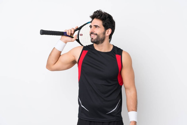 Joven hombre guapo con barba sobre fondo blanco aislado jugando tenis y mirando hacia arriba
 - Foto, Imagen