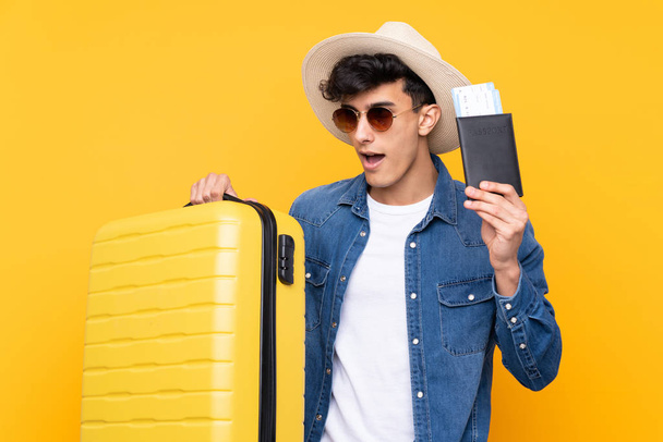 Arjantinli genç adam izole edilmiş sarı arka planda tatilde bavul ve pasaportla - Fotoğraf, Görsel