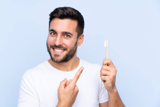 Giovane bell'uomo con la barba lavarsi i denti su sfondo isolato che punta verso il lato per presentare un prodotto
 - Foto, immagini
