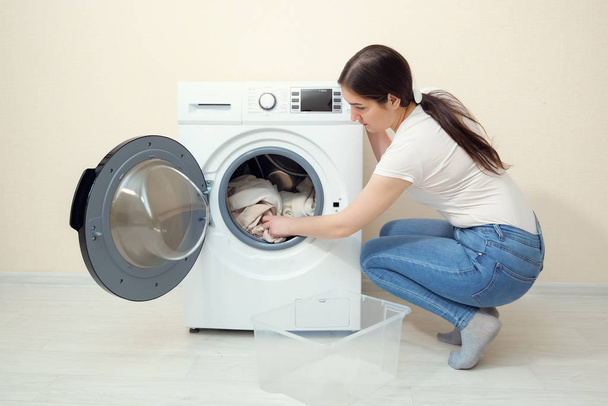 mujer carga ropa sucia en lavadora cerca de la pared beige
 - Foto, imagen