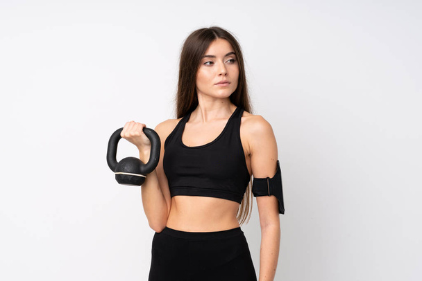 Jonge sport vrouw over geïsoleerde witte achtergrond maken gewichtheffen met kettlebell - Foto, afbeelding