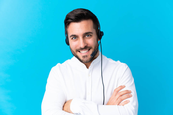 Telemarketer man werken met een headset over geïsoleerde blauwe achtergrond lachen - Foto, afbeelding