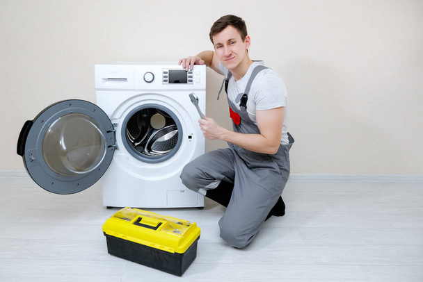 meester met moersleutel bij wasmachine tegen beige wand - Foto, afbeelding