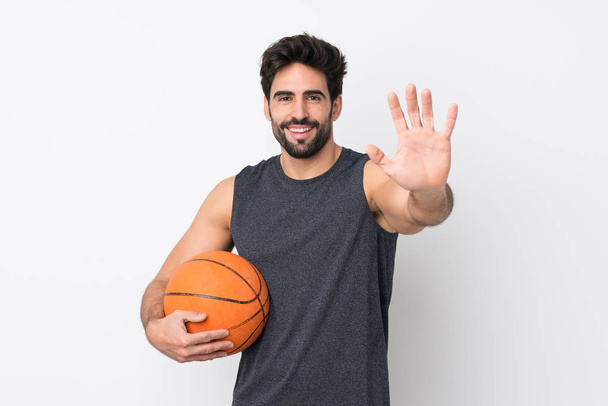 Basketball player man with beard over isolated white background saluting with hand with happy expression - Photo, Image