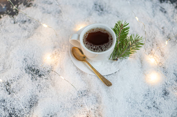Біла чашка з гарячою кавою. Піднімається штучним снігом. Біля гілки ялини. Новорічно різдвяний
. - Фото, зображення