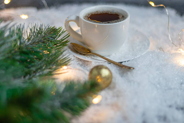 White cup with hot coffee. Stands in artificial snow. Near a branch of spruce. New Year's and Christmas. - Foto, Bild