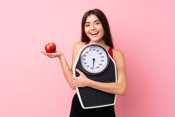 Menina bonita com máquina de pesagem sobre fundo rosa isolado com máquina de pesagem e com uma maçã - Foto, Imagem