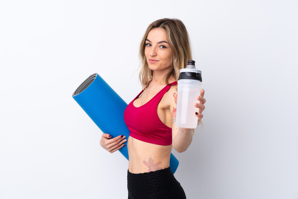 Young sport woman over isolated white background with sports water bottle and with a mat - Photo, Image