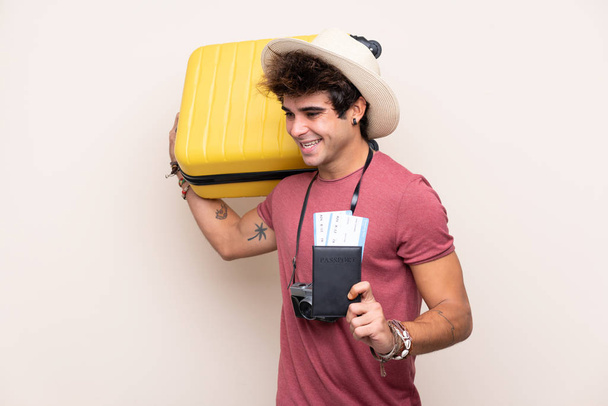 Jonge blanke man over geïsoleerde achtergrond in vakantie met koffer en paspoort - Foto, afbeelding