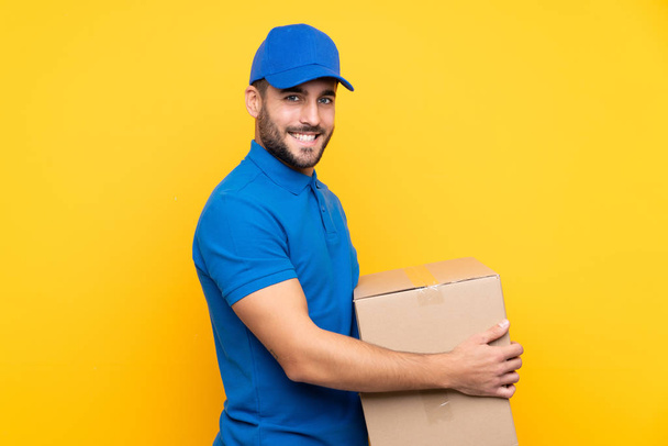 Delivery man over isolated yellow background smiling a lot - Foto, afbeelding