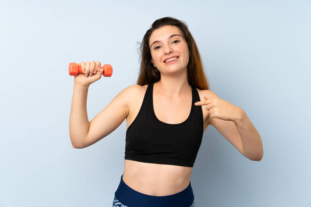 Giovane donna sportiva con sollevamento pesi su sfondo blu isolato con espressione facciale a sorpresa
 - Foto, immagini