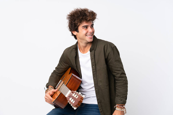 Молодой кавказский человек с гитарой на изолированном белом фоне смотрит в сторону
 - Фото, изображение