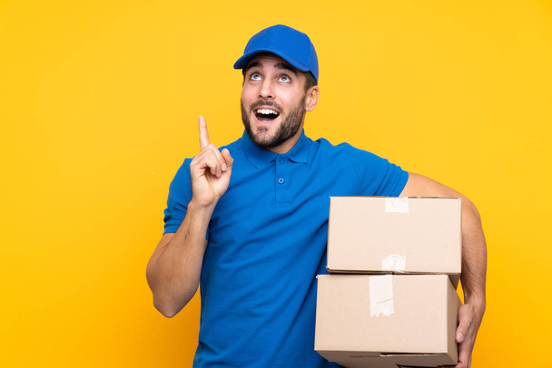 Delivery man over isolated yellow background intending to realizes the solution while lifting a finger up - Photo, Image