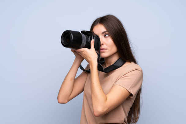 Mladá žena přes izolované modré pozadí s profesionální kamerou - Fotografie, Obrázek