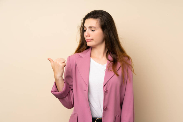Young brunette girl with blazer over isolated background unhappy and pointing to the side - Photo, Image