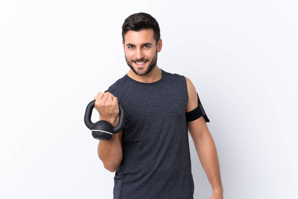 Jonge sport knappe man met baard over geïsoleerde witte achtergrond maken gewichtheffen met kettlebell - Foto, afbeelding