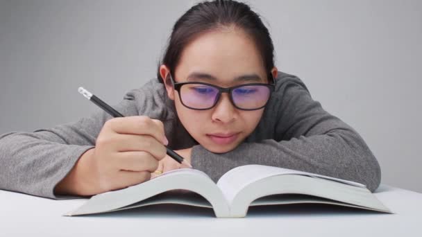 Νεαρή γυναίκα με γυαλιά που σχεδιάζει μια γραμμή και γράφει μια σύντομη περίληψη ενώ διαβάζει ένα βιβλίο στη βιβλιοθήκη. - Πλάνα, βίντεο