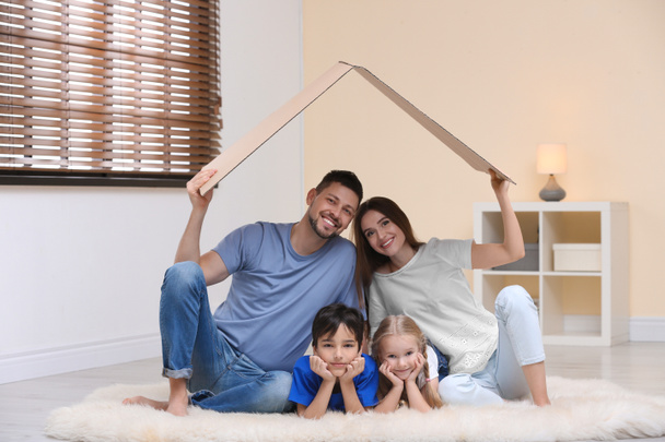 Happy family sitting under cardboard roof at home. Insurance con - 写真・画像
