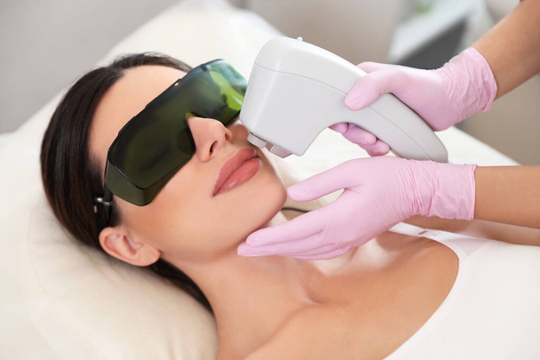 Young woman undergoing laser epilation procedure in beauty salon - Foto, imagen