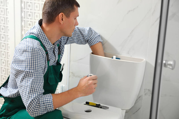 Professional plumber repairing toilet bowl in bathroom - Foto, afbeelding