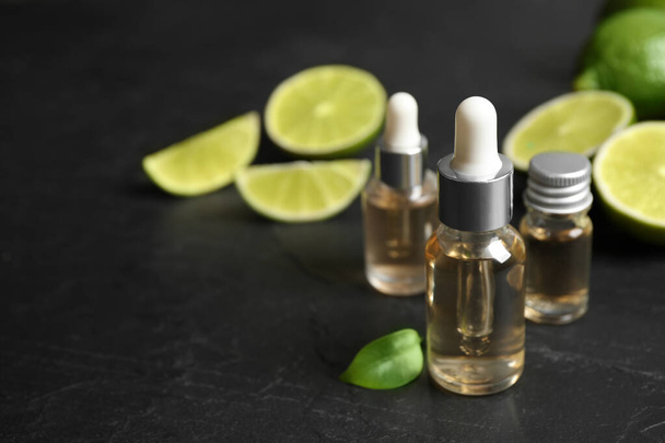 Lime essential oil and cut citrus fruits on black table. Space for text - Photo, Image