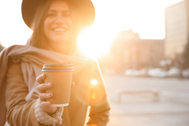 Young woman with cup of coffee on city street in morning, focus  - Foto, Imagen
