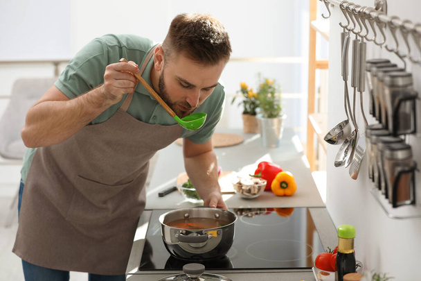 Young man cooking delicious soup in kitchen - Foto, immagini