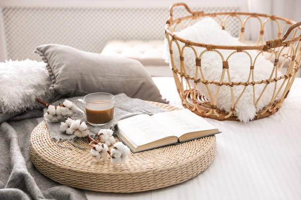 Composition with cup of drink, cotton and book on wicker pouf indoors - Fotografie, Obrázek
