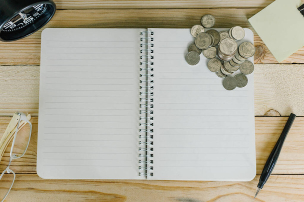 Concepto de planificación financiera, bloc de notas, moneda, vasos y despertador en mesa de madera
. - Foto, imagen