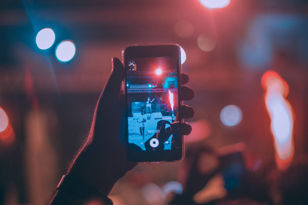 рука держит смартфон и записывает видео во время концерта
 - Фото, изображение