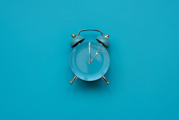 Time to eat. Plate with cutlery as clock on blue background. Top view. Flat lay. Weight loss and diet concept - Photo, image