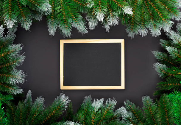 Christmas or New Year decoration on dark background: fir-tree branches, and drawing board. Banner mockup, postcard. Flat lay, top view - Fotografie, Obrázek