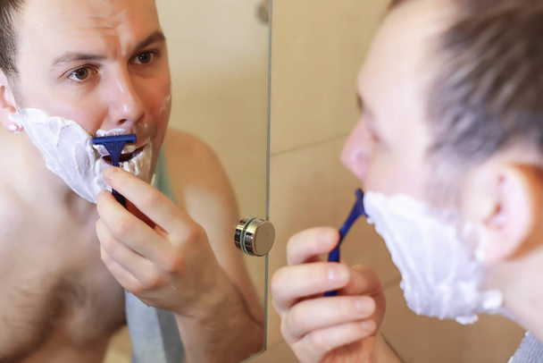 Ένας άντρας ξυρίζεται στο μπάνιο το πρωί. - Φωτογραφία, εικόνα
